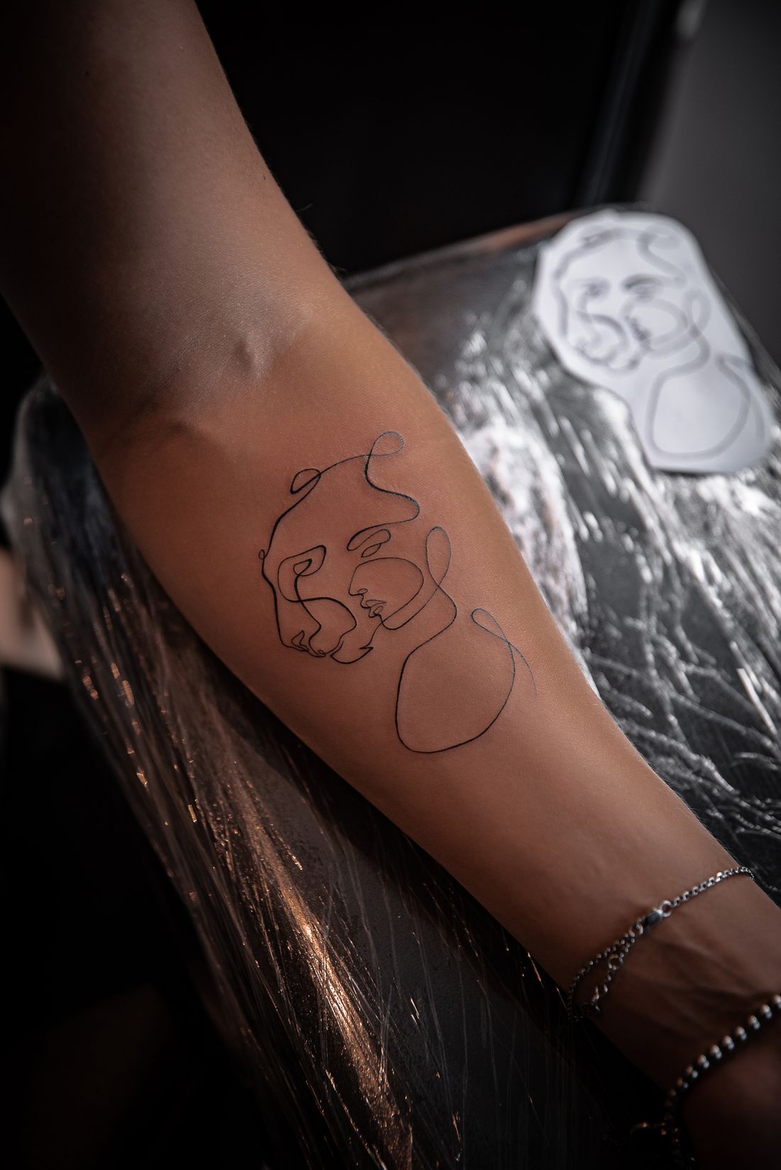 Tatuagem de dois rostos desenhados com uma linha fina no antebraço