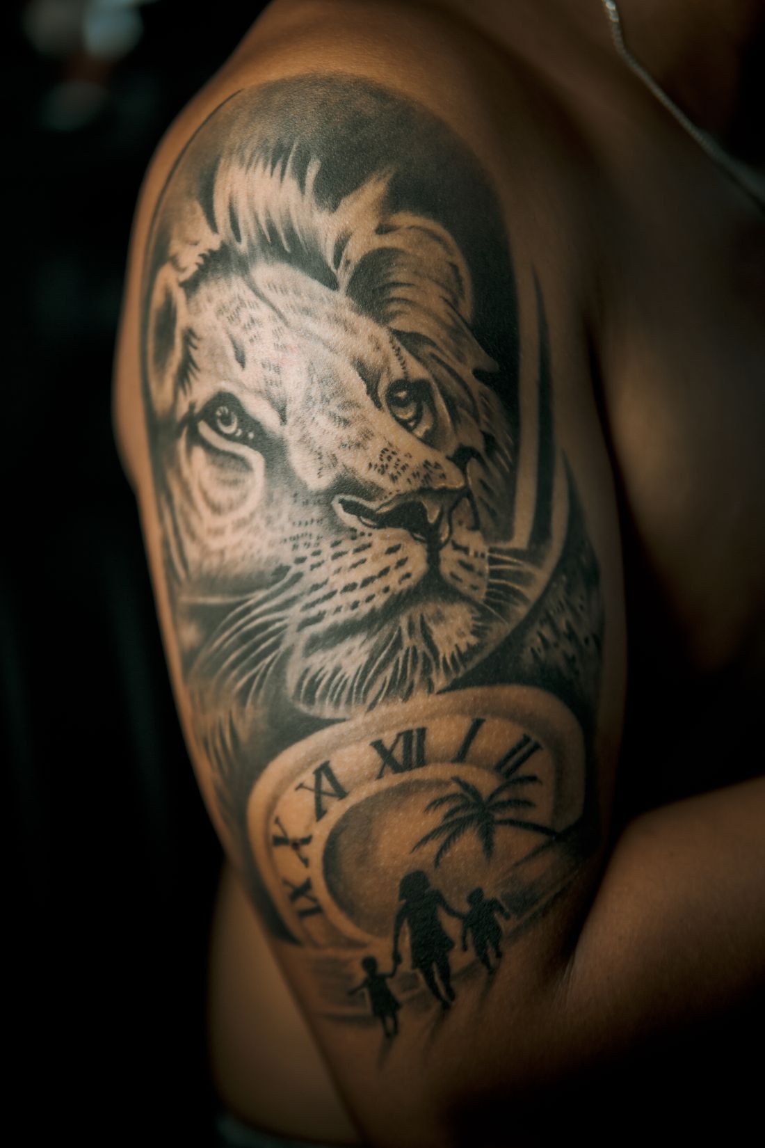 Tatuagem realista de um leão com um relógio e silhuetas de uma família no braço