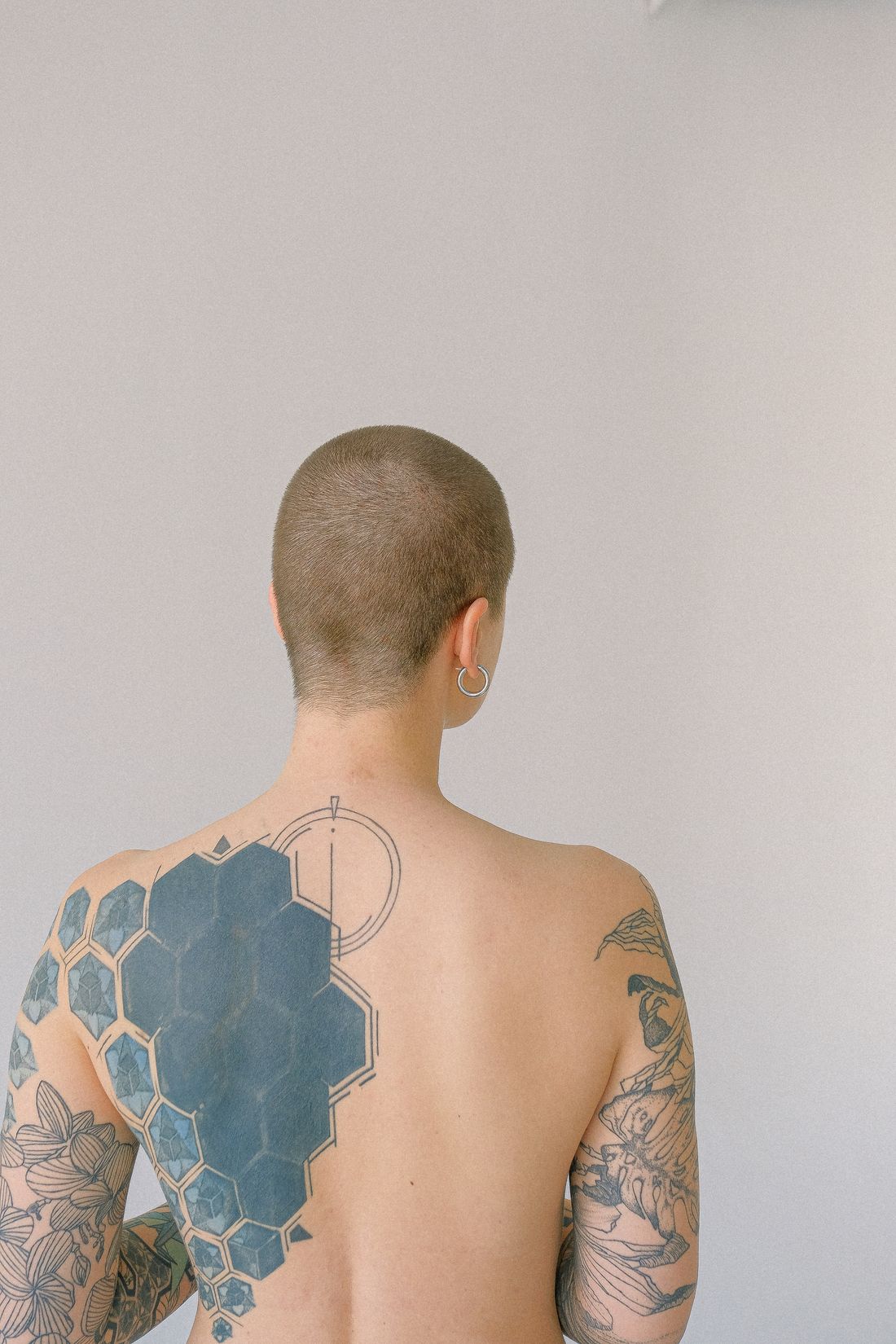 Composição geométrica de hexágonos e motivos botânicos tatuados nas costas e nos braços